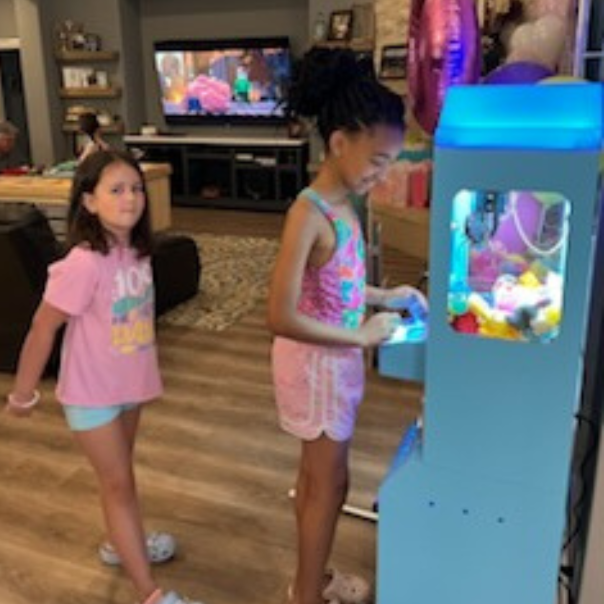 Kids gathered around a claw machine at a birthday party, watching and playing together.