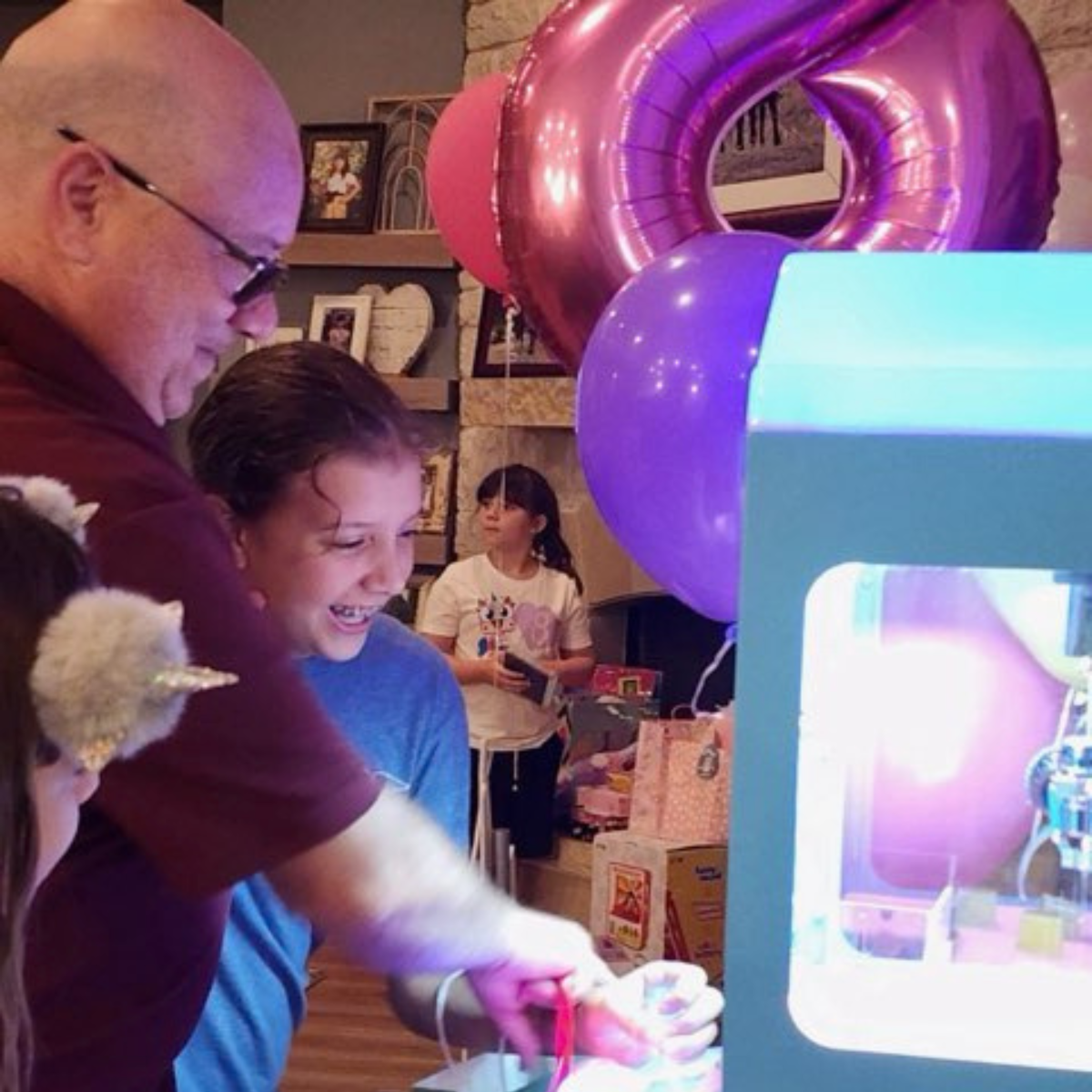 Dad helping his child play a claw machine at a birthday party, creating a fun family moment.